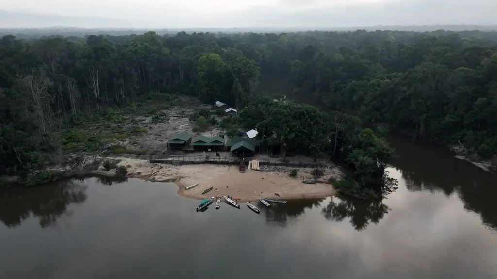 圭亞那埃塞奎博河沙岸上的叢林釣魚營地航拍，綠色屋頂的營舍與停靠的小艇清晰可見