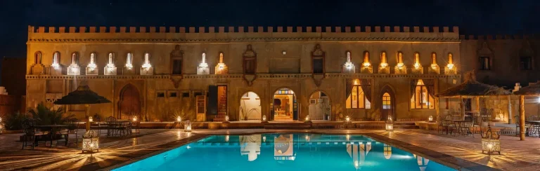 Kasbah-style hotel with a lit swimming pool in the evening