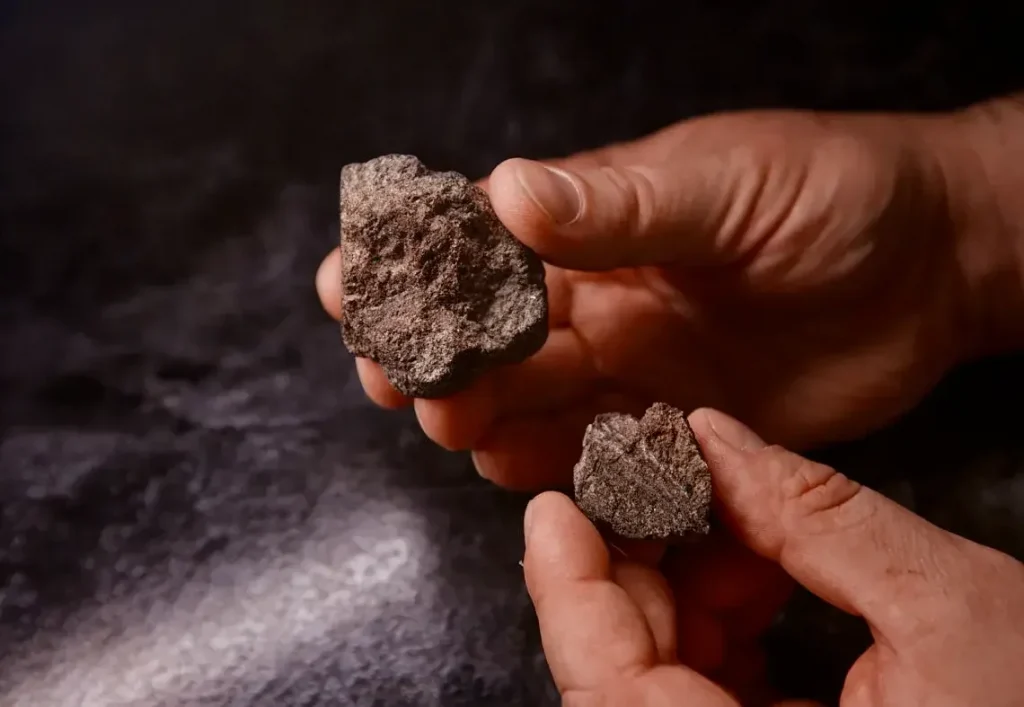 Hands holding two rough meteorite fragments