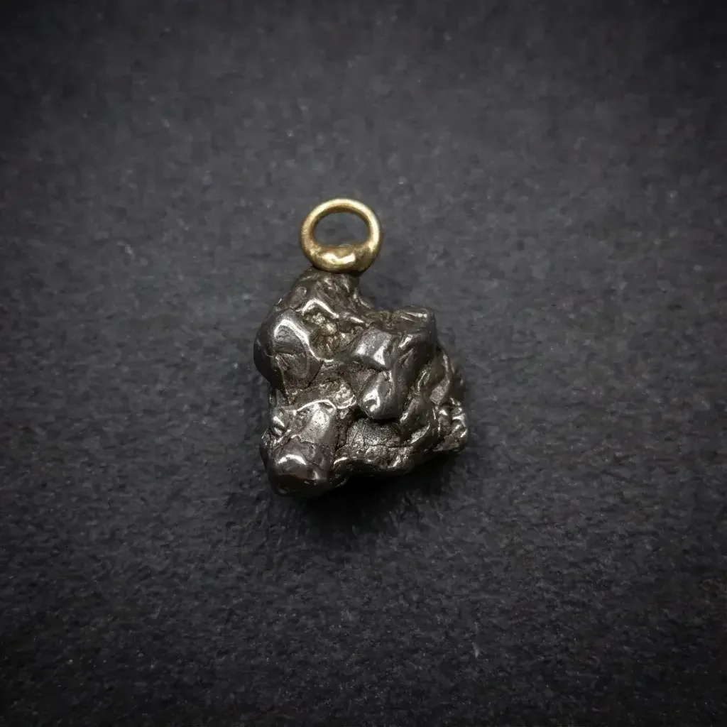Small meteorite fragment on a ring pendant on a dark surface